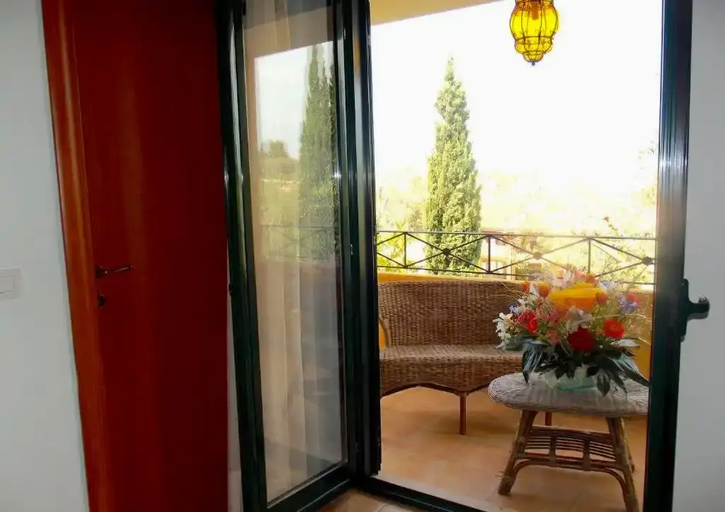 Porta finestra aperta su un balcone con piante e fiori su un tavolino.
